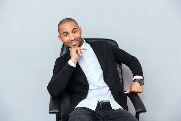 Zelfverzekerde lachende Afro-Amerikaanse jonge man zitten in de stoel van het Bureau — Stockfoto