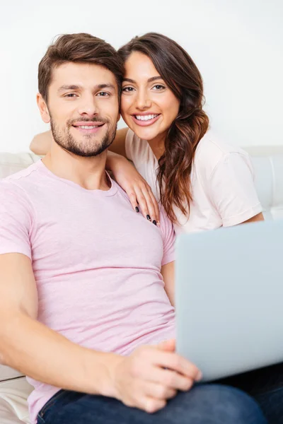 Happy young couple sitting on couch using laptop — Stock Photo, Image