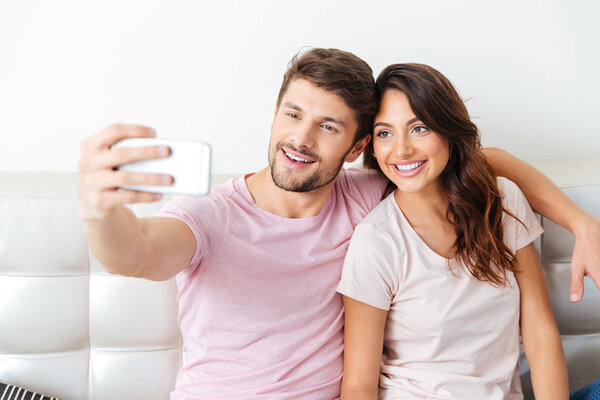 Happy couple smiling and taking selfie on the couch