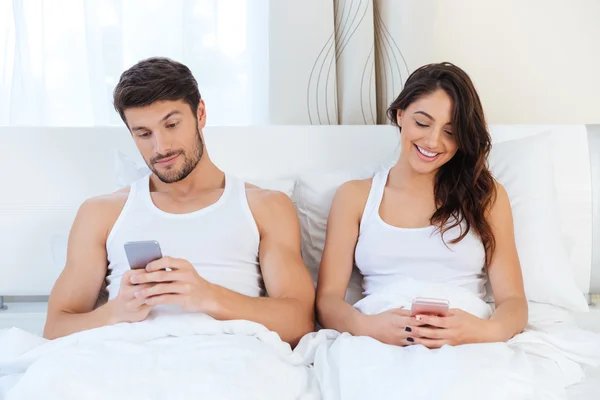 Ευτυχισμένο ζευγάρι σε ένα κρεβάτι με τα κινητά τηλέφωνα — Φωτογραφία Αρχείου