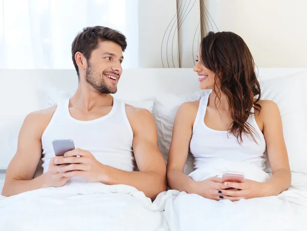 Couple heureux dans un lit avec téléphones mobiles — Photo