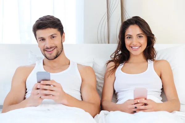 Happy couple in a bed with mobile phones — Stock Photo, Image