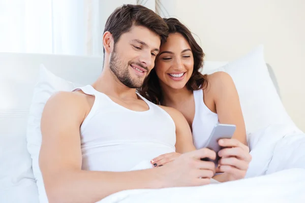 Joven pareja dulce en la cama mirando un teléfono móvil — Foto de Stock