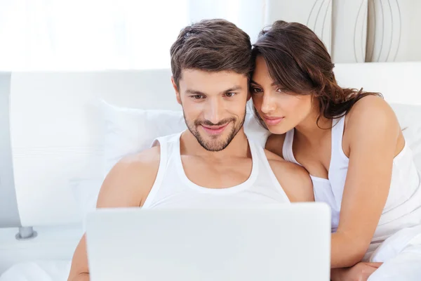 Beautiful young couple looking at laptop in bed — Stock Photo, Image