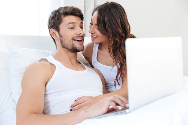 Sonriente pareja joven utilizando el ordenador portátil en la cama — Foto de Stock