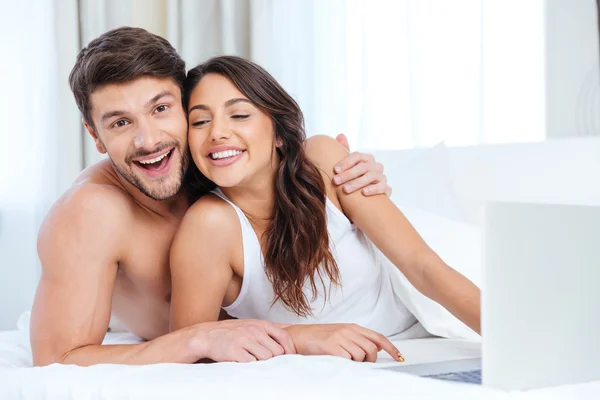 Beautiful young couple using laptop and looking at camera — Stock Photo, Image