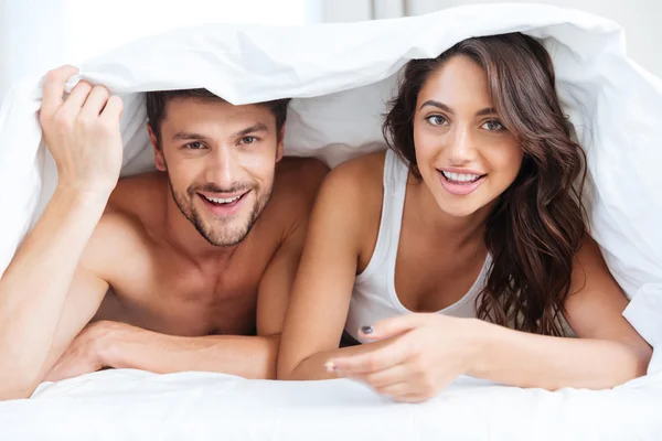 Happy couple lying in bed covered with blanket at home Royalty Free Stock Images