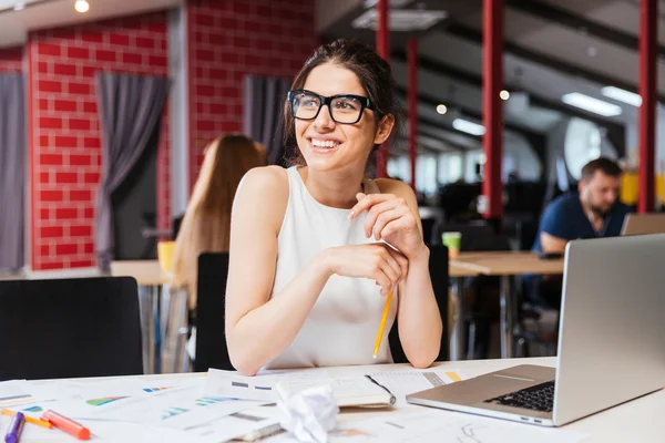 Sonriendo bastante joven mujer de negocios en gafas sentado en el lugar de trabajo —  Fotos de Stock