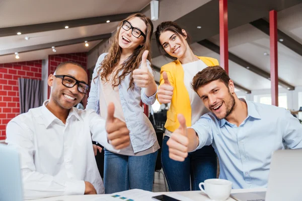 Smiling business people showing thumbs up working in office — Stock Photo, Image