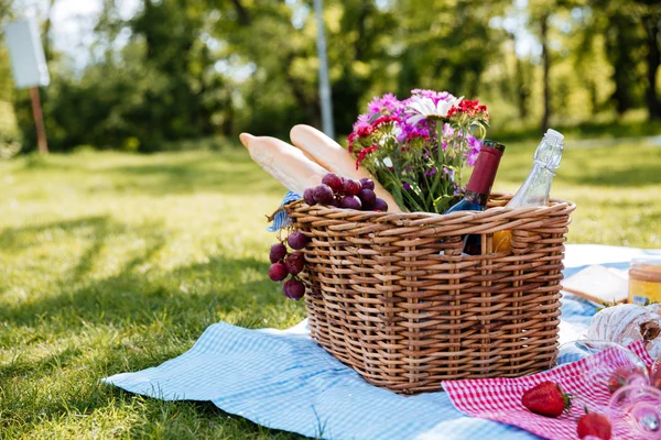 Cesta de piquenique com bebidas, alimentos e flores na grama — Fotografia de Stock