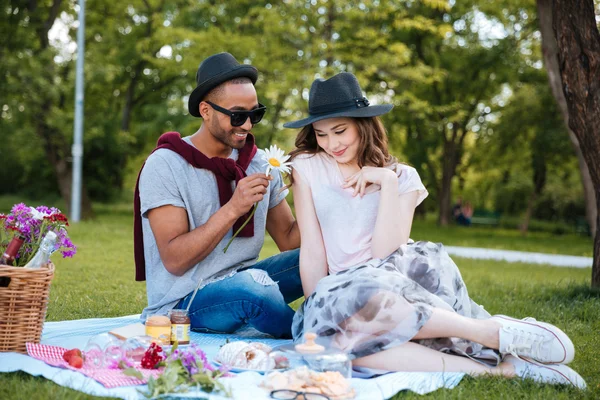 Sonriente joven dando flores a su novia en el picnic — Foto de Stock