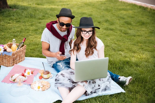 Pareja de picnic y el uso de ordenador portátil en el parque — Foto de Stock