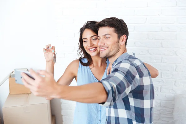 Casal jovem fazendo selfie segurando chaves em novo apartamento — Fotografia de Stock