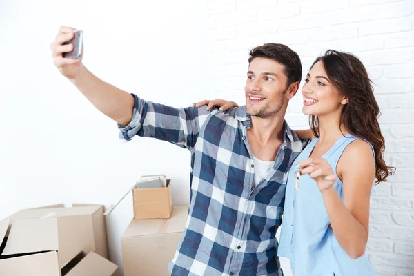 Pareja joven haciendo selfie sosteniendo llaves en nuevo piso —  Fotos de Stock