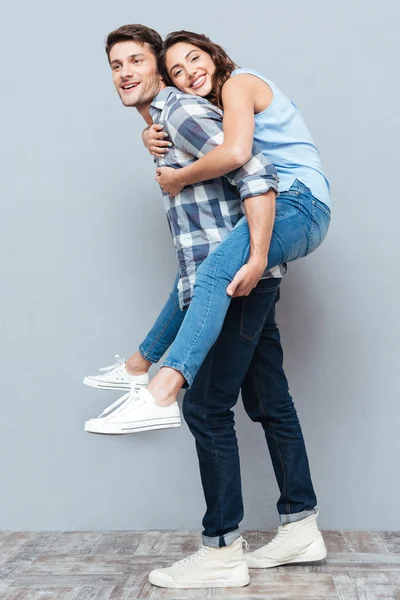 Junges Paar genießt Huckepackfahrt über grauen Hintergrund — Stockfoto