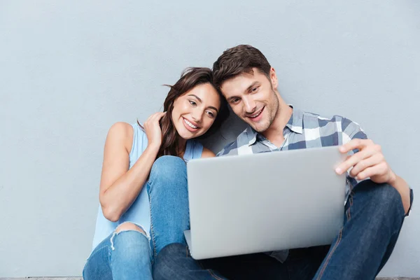 Retrato de feliz pareja joven usando portátil sobre fondo gris —  Fotos de Stock