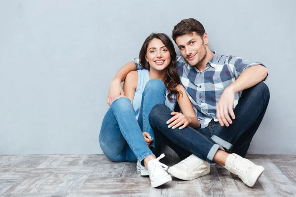 年轻幸福的夫妇坐在地板上灰色 bakground — 图库照片