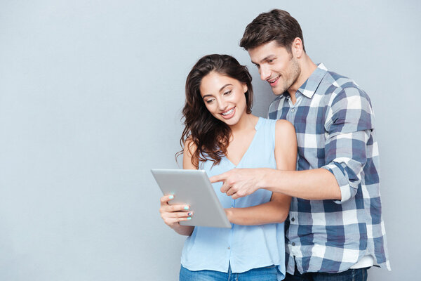 Young couple pointing at pc tablet over gray background
