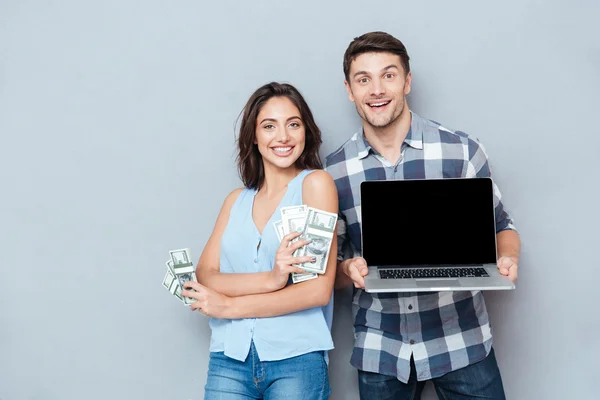 快乐的年轻夫妇，在灰色的背景使用笔记本电脑的肖像 — 图库照片