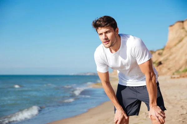 Мужчина в белой футболке и шортах стоит на пляже — стоковое фото
