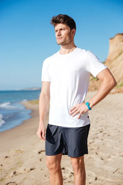 Nachdenklicher junger Sportler steht und denkt am Strand — Stockfoto