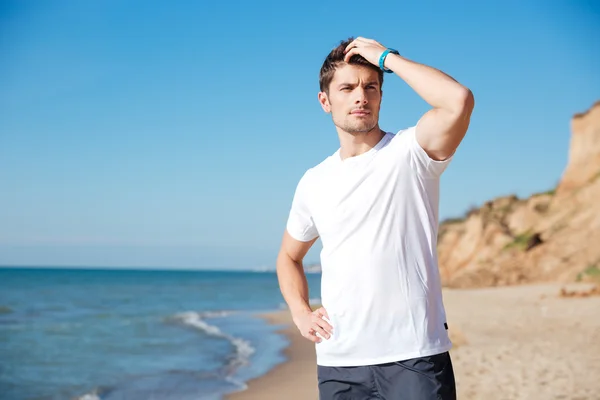 Jeune homme attrayant debout et réfléchissant sur la plage — Photo