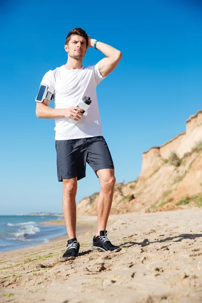 Atractivo joven deportista con botella de agua en la playa —  Fotos de Stock