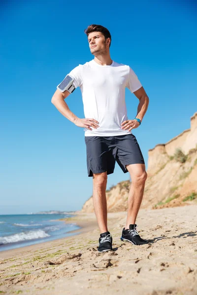 Attractive young sportsman with cell phone standing on the beach — Stock Photo, Image