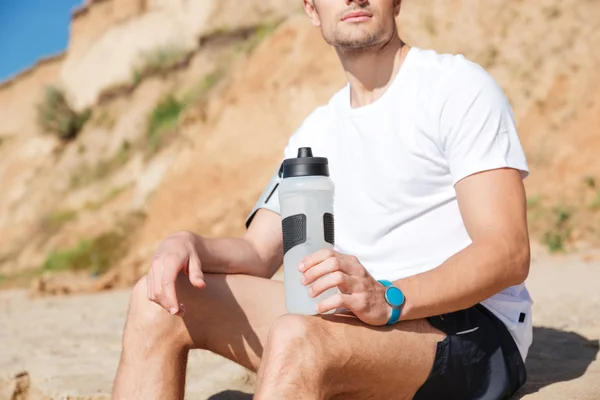 Sportsman med flaska vatten sitter på stranden — Stockfoto