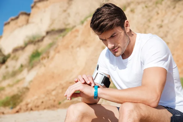 Deportista sentado y usando un rastreador de fitness en la playa — Foto de Stock