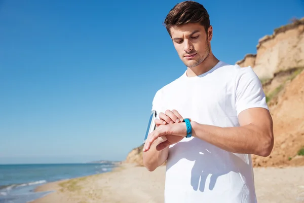 Deportista de pie y usando reloj inteligente en la playa — Foto de Stock