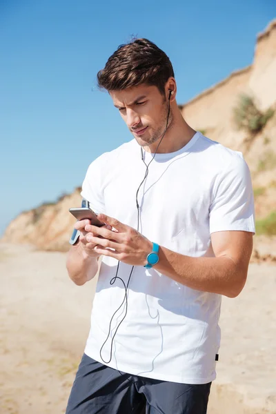 นักกีฬาฟังเพลงจากโทรศัพท์มือถือบนชายหาด — ภาพถ่ายสต็อก