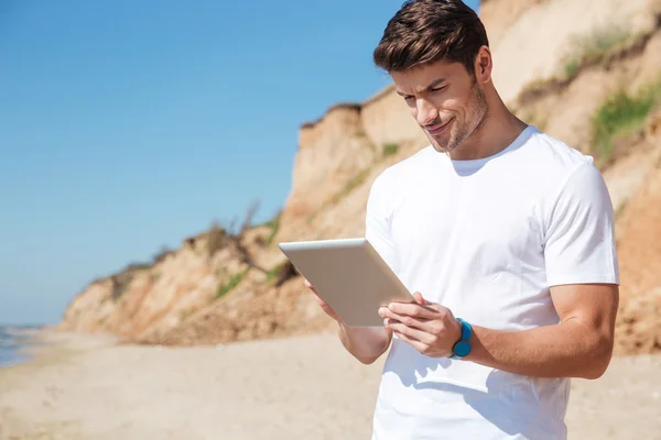 Χαρούμενος νεαρός άνδρας χρησιμοποιώντας tablet στην παραλία — Φωτογραφία Αρχείου