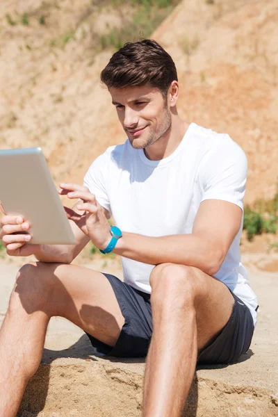 Χαμογελαστός νεαρός άνδρας χρησιμοποιώντας tablet στην παραλία — Φωτογραφία Αρχείου