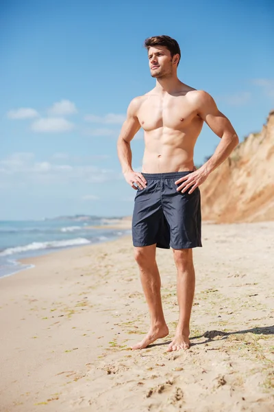 Jovem atlético confiante em pé na praia — Fotografia de Stock