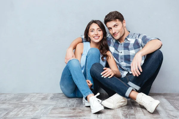 Jovem casal feliz sentado no chão sobre terreno cinzento — Fotografia de Stock