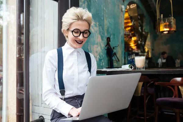 Beautiful young woman in glasses working on laptop and smiling — Stock Photo, Image