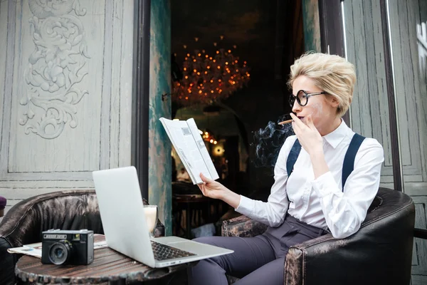 Пенсионерка пользуется ноутбуком и читает журнал в кафе — стоковое фото