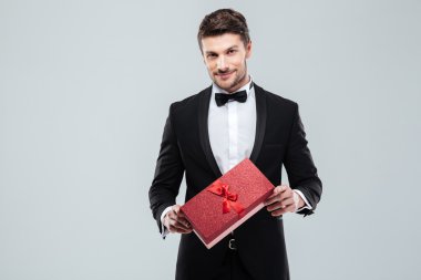 Kendinden emin attracive adam ayakta ve hediye kutusu tutarak smokin