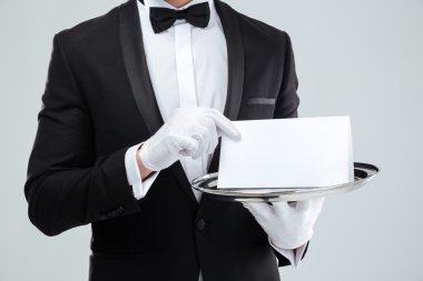 Butler in tuxedo and gloves holding blank card on tray clipart
