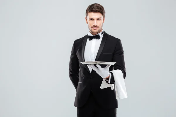 Гарний офіціант у смокінгу та рукавичках, що тримають порожній лоток — стокове фото