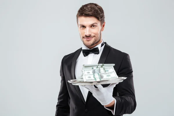 Camarero sonriente en esmoquin y guantes sosteniendo bandeja con dinero — Foto de Stock