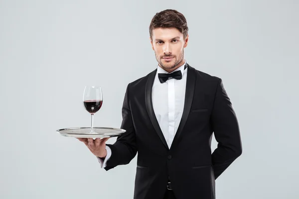 Официант в смокинге держит бокал красного вина на подносе — стоковое фото