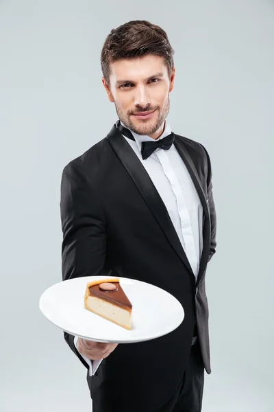 Butler in tuxedo holding piece of cake on plate — Stock Photo, Image