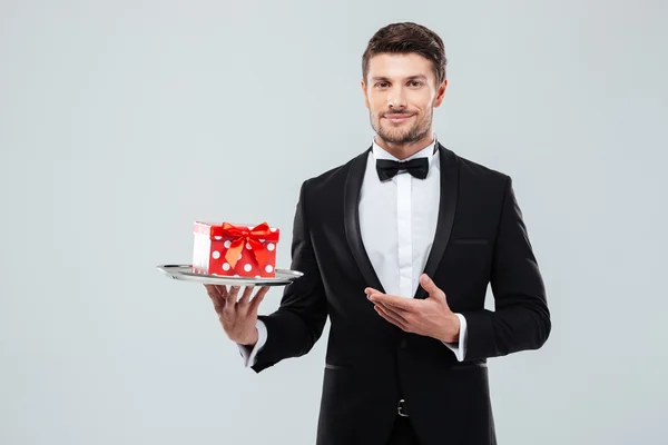 Официант в смокинге стоит и держит коробку с подарками на подносе — стоковое фото