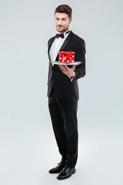 Butler em smoking de pé e segurando bandeja com caixa de presente — Fotografia de Stock
