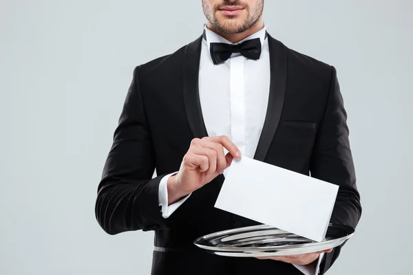 Waiter in tuxedo with bowtie holding blank card on tray — Stock Photo, Image