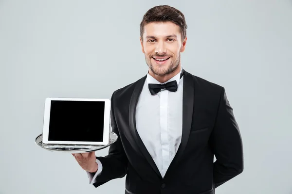 Cheerful waiter in tuxedo holding blank screen tablet on tray — Stock Photo, Image