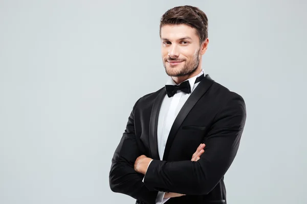 Zelfverzekerde man in smoking staande glimlachend met gekruiste armen — Stockfoto