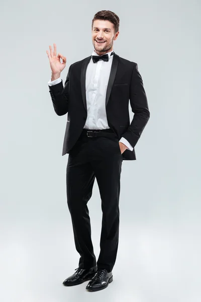 Cheerful young man in tuxedo with bowtie showing ok sign — Stock Photo, Image